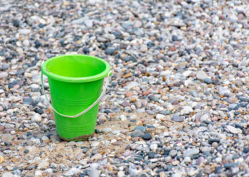 Green toy bucket on pebble beach