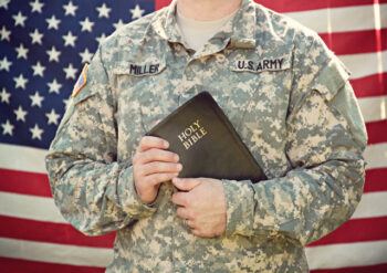 American military person holding Holy Bible standing in front of American flag