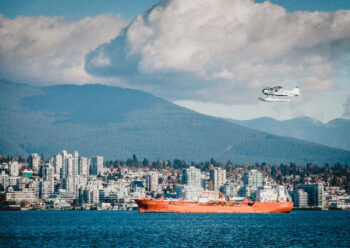 Water plane in flight over water with city and mountains to its side