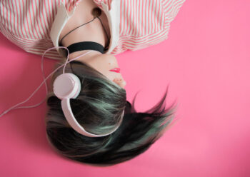 Female laying down wearing headphones with pink background