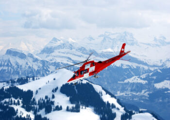 Red and white helicopter flying near snow covered mountains