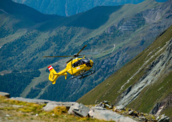 Yellow helicopter flying close to mountain side